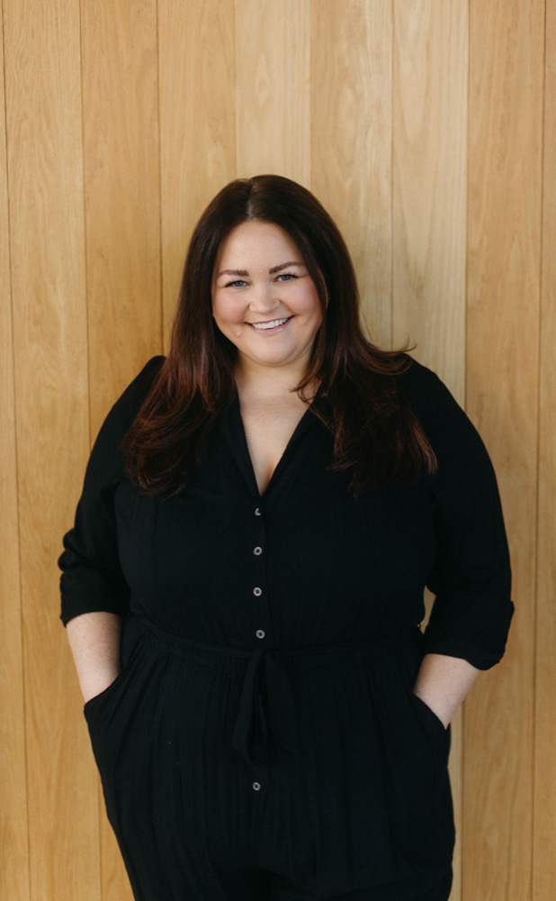 Katie Sanders smiling, standing against a wood-paneled wall