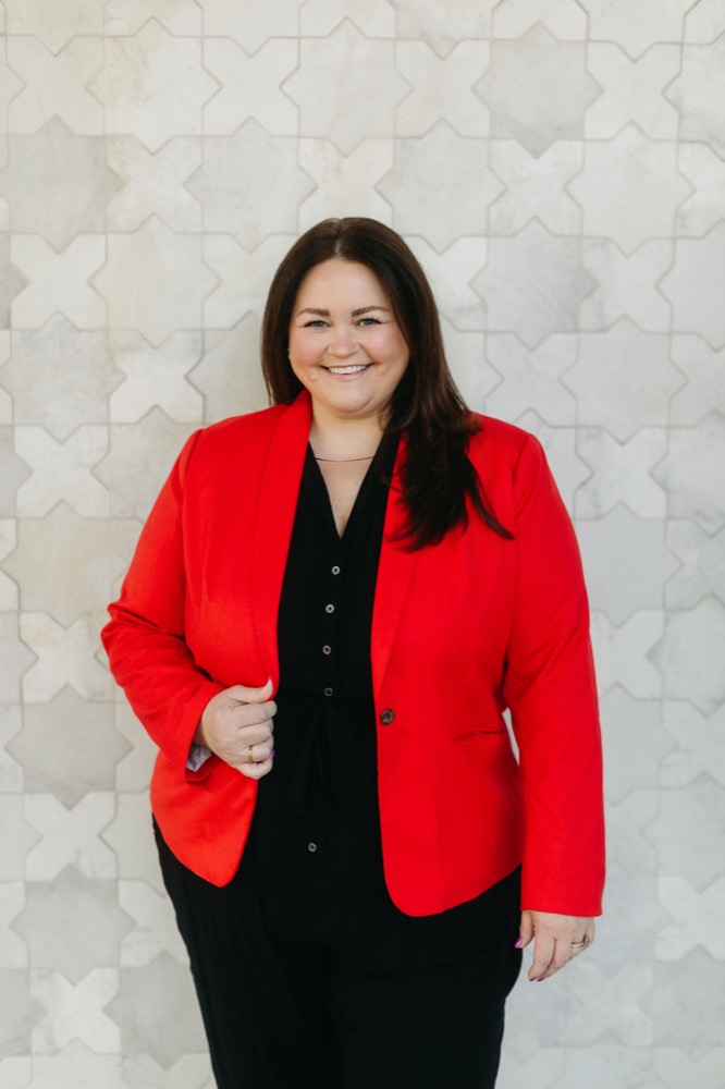 Katie Sanders smiling, wearing a red blazer